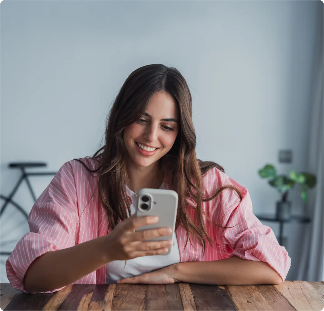 A woman smiling at her phone at a kitchen table