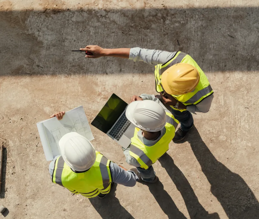 Three workers in hard hats gathered around a tablet on a concrete slab