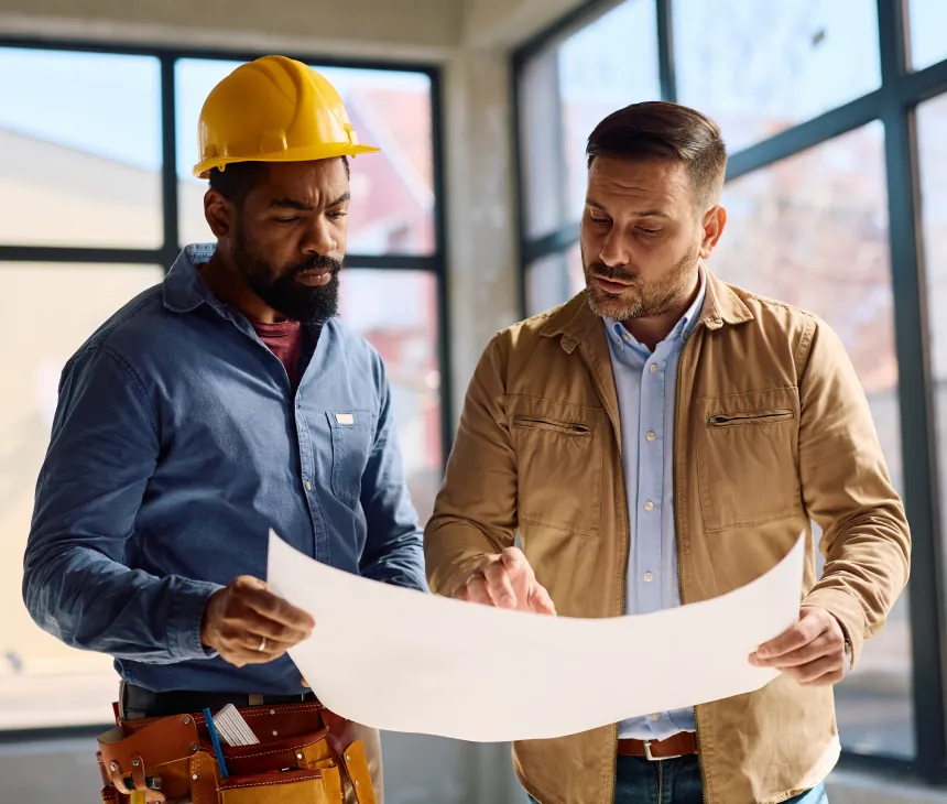 Two tradespeople on site reviewing a large paper drawing