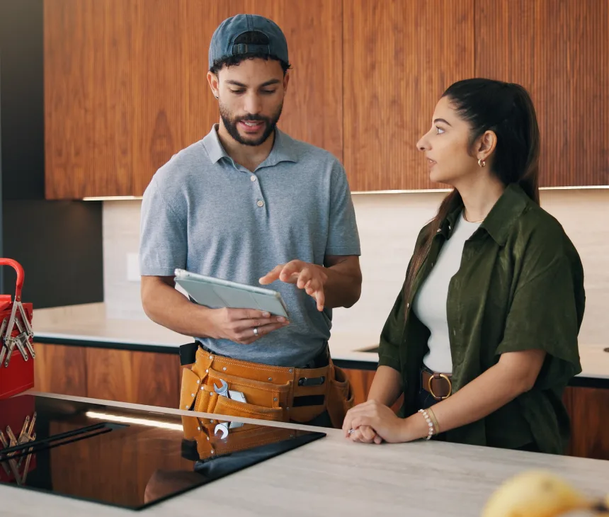 A service technician with a tool belt showing a tablet to a customer across a kitchen counter