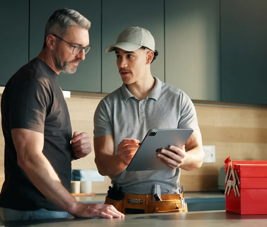 Two service technicians reviewing a job on a tablet in a customer home