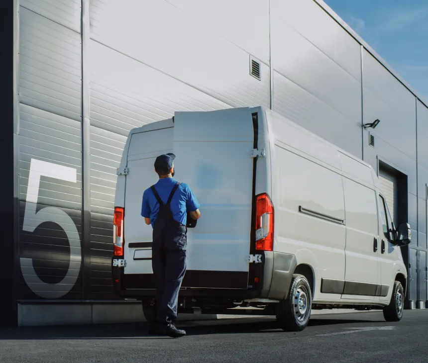 A driver at the rear of a white van backed onto a loading bay