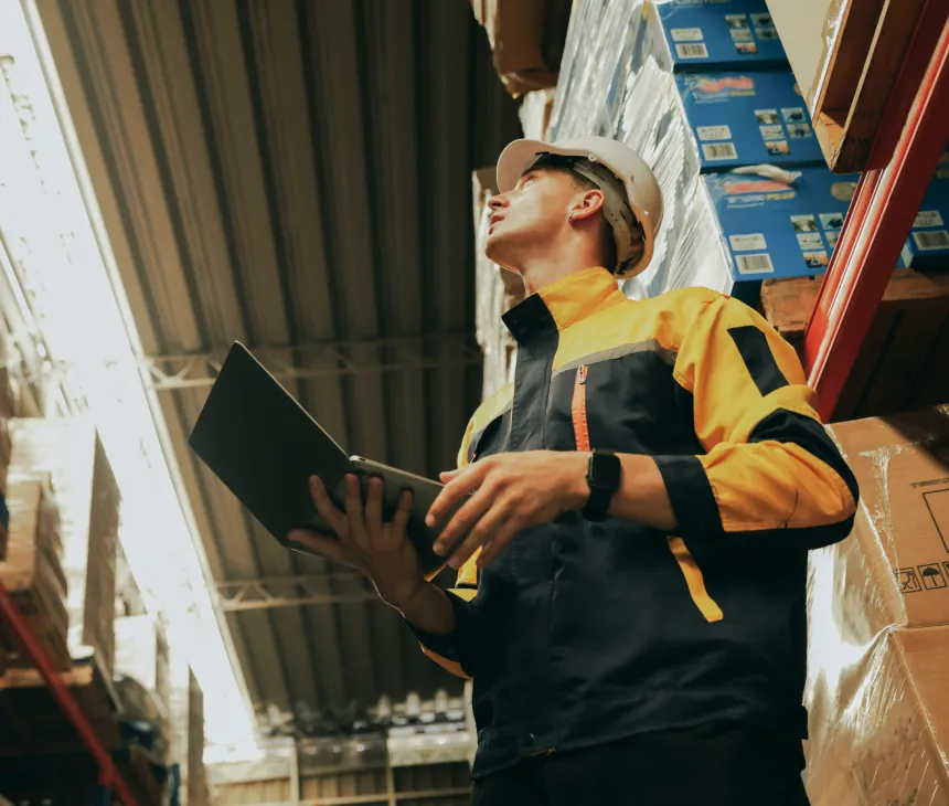 A warehouse worker reviewing a laptop beside pallet racking