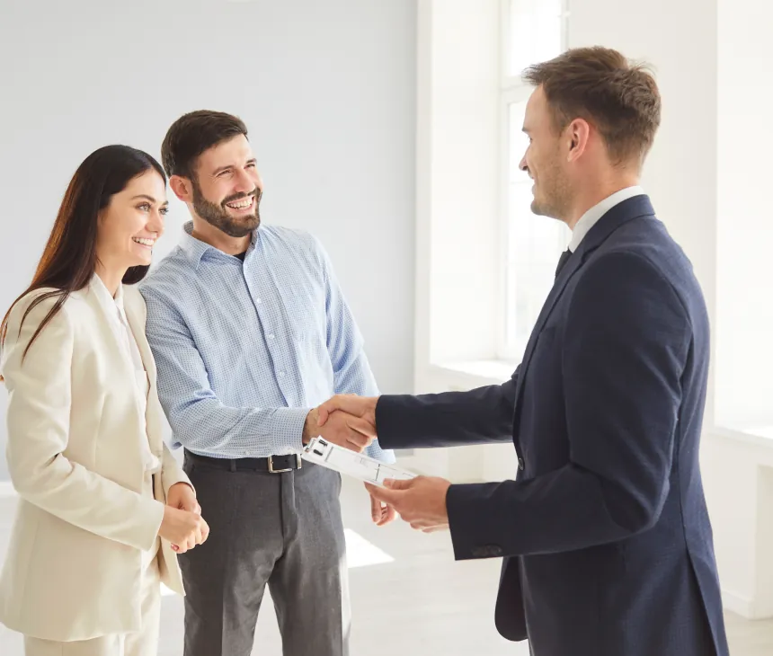 A couple shaking hands with an agent in a bright empty room