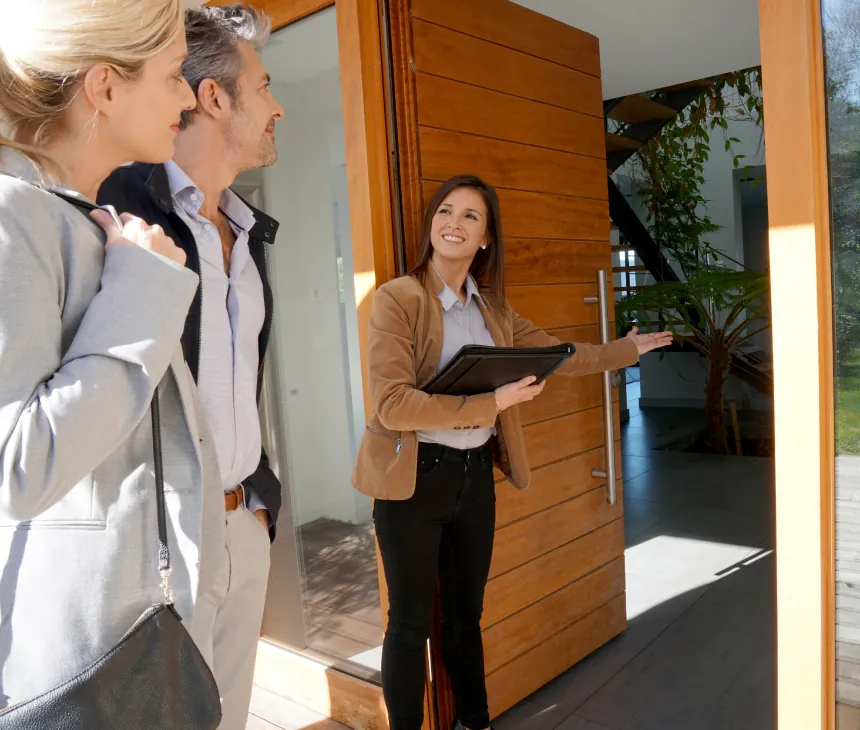 An agent with a tablet greeting visitors at the door of a property