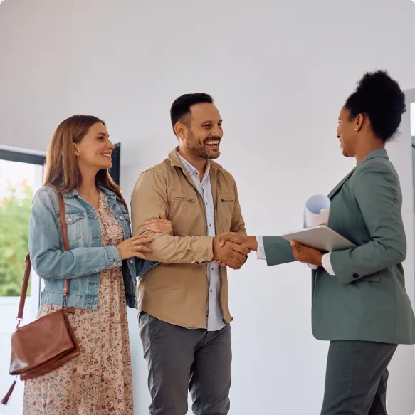 A letting agent holding a tablet shaking hands with a couple in a bright room